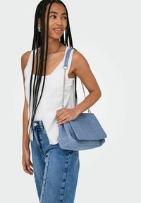 Borsa a mano azzurro chiaro con patta ripiegabile e tracolla in metallo argentato. Il tessuto ha una finitura testurizzata, arricchita da un design strutturato.