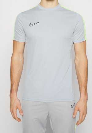 Man draagt een lichtgrijze Nike sportoutfit met neongroene strepen op de schouders en zwarte Nike-logo's op de borst en korte broek.