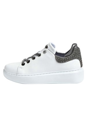 Biała sneaker z grubą podeszwą, czarnymi sznurówkami i błyszczącym srebrnym detalem na pięcie, widziana z boku na jednolitym tle.