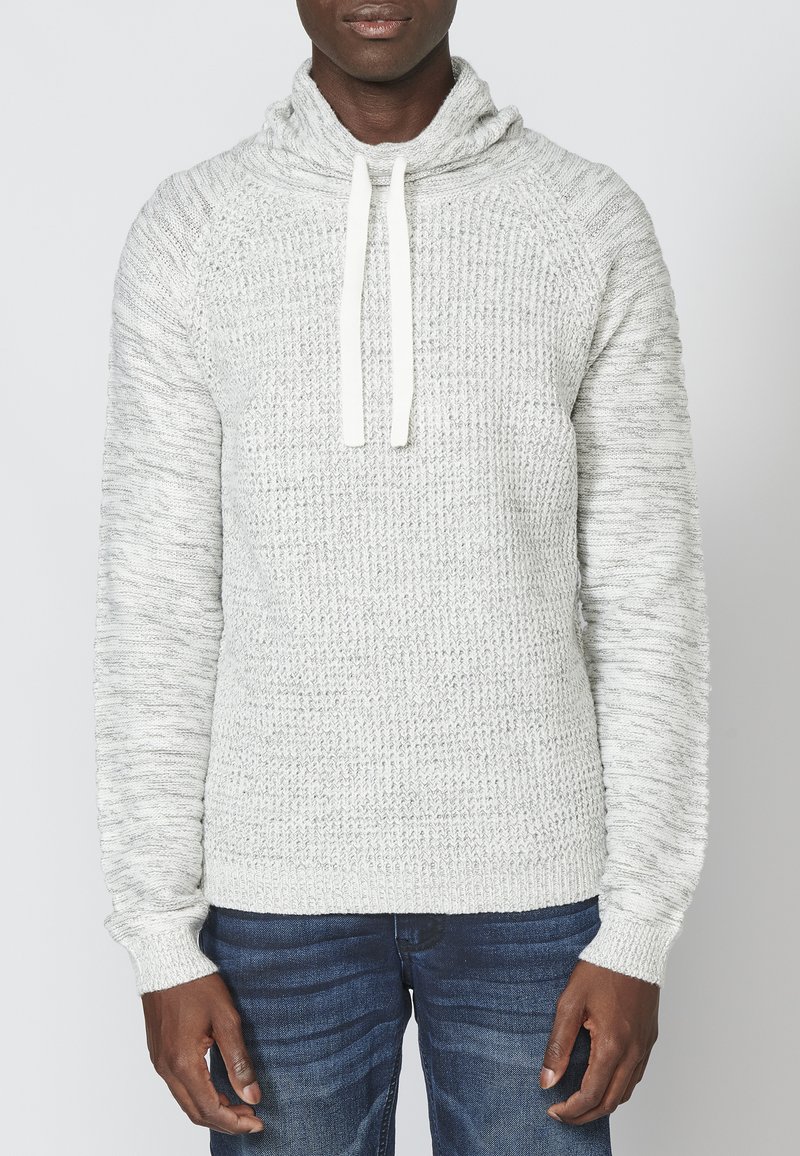 Hellgrauer Pullover mit Schalkragen und Kordelzügen. Stricktextur, gerippte Bündchen und Saum, mit einem leicht lockeren Schnitt. Kombiniert mit dunklen Jeans.