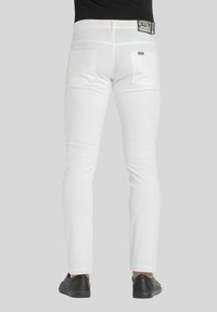 Jeans bianchi aderenti con tasche posteriori, abbinati a scarpe nere. Il tessuto ha una texture liscia e un design pulito, con cuciture sottili.