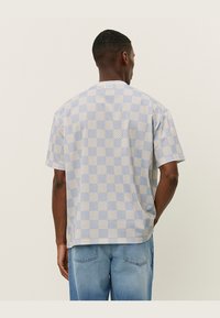 Short-sleeve shirt featuring a light blue and beige checkerboard pattern, crafted from a breathable textured fabric, with a relaxed fit and round neckline.