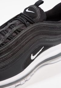 Detailní záběr na černý tenisek Nike Air Max s bílým logem Swoosh, černými tkaničkami a viditelným vzduchovým polstrováním v bílé podrážce.