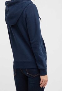 Felpa con cappuccio blu navy, dotata di tasca a marsupio, polsini e orlo a costine, realizzata in tessuto morbido. Presenta una tasca con zip sul lato.
