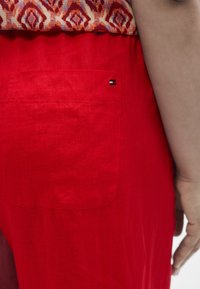 Close-up of a person wearing a red skirt with a back pocket, an orange patterned top visible, and their right arm resting by their side.