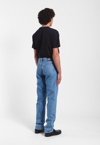 Černé tričko s krátkým rukávem v kombinaci se světlomodrými rovnými džíny. Materiál vypadá jako denim, má hladkou texturu a mírné odbarvení. Přidány černé boty.