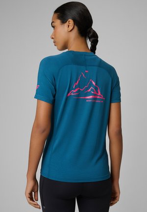 Młoda kobieta z ciemnymi warkoczami, ubrana w turkusową koszulkę turystyczną z różową grafiką góry i napisem „Never Stop Hiking” na plecach.