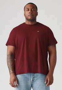 Bordeaux bomulds t-shirt med korte ærmer og rund hals, med et lille hvidt logo på brystet. Båret med lyseblå denim jeans.