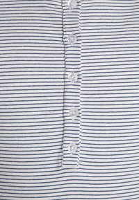 Koszula zapinana na guziki w granatowo-białą paski, wykonana z miękkiego materiału, z pięcioma okrągłymi przezroczystymi guzikami wzdłuż pliski.