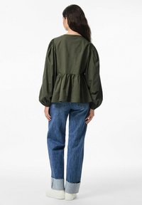 Top peplum in cotone verde oliva con maniche a palloncino, abbinato a jeans in denim blu chiaro con risvolto e orlo sfilacciato.