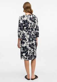 Blumendruckkleid mit einem schwarz-weißen Muster, Dreiviertelärmeln und taillierter Passform, knielang und aus glattem Stoff.