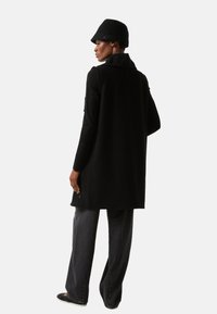 Sort, langærmet cardigan med krave, lavet af et tekstureret stof. Kombineret med løstsiddende mørke jeans og en matchende sort bucket hat.