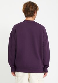 Sweatshirt violet avec une coupe décontractée, un col rond et des poignets côtelés. Le tissu semble doux avec une texture lisse. Pas de logos ou motifs visibles.