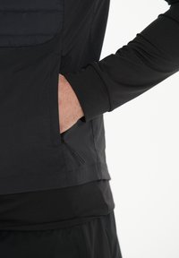 Schwarze Sportjacke mit Reißverschluss-Tasche, glattem Stoff und langen Ärmeln. Verfügt über ein gestepptes Schulterpanel und eine taillierte Passform.