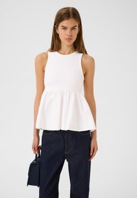 Top bianco senza maniche con un corpetto aderente e un orlo peplum svasato, abbinato a jeans blu scuro e una piccola borsa rettangolare.