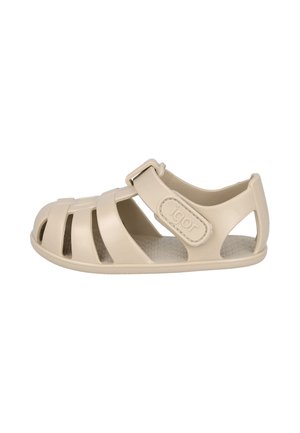 Sandalia beige para niño con puntera cerrada, correa ajustable de velcro y diseño recortado, plantilla texturizada y nombre de la marca "igor" en la correa.