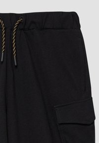 Schwarze Baumwoll-Jogginghosen mit einem elastischen Bund und kontrastierenden goldenen Kordeln. Mit einer seitlichen Cargo-Tasche mit Klappen-Detail.