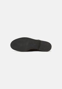Suola di scarpa nera in gomma con scanalature e creste texture, che mette in evidenza un design piatto. Un minimo di branding è visibile sulla superficie.