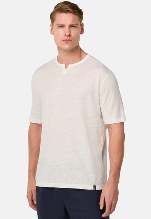 T-shirt bianco a maniche corte realizzato in tessuto testurizzato, con scollatura henley caratterizzata da una piccola apertura e un orlo leggermente curvo.