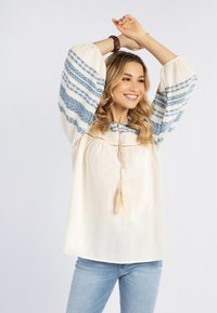 Blusa leggera in crema con maniche a motivo blu e una chiusura con nappina. Presenta maniche a palloncino e una vestibilità rilassata.