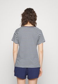 Camiseta a rayas en azul marino y crema, de manga corta, fit relajado. Combinada con pantalones cortos azul marino, de tela de algodón. Diseño simple, sin patrones o acentos notables.