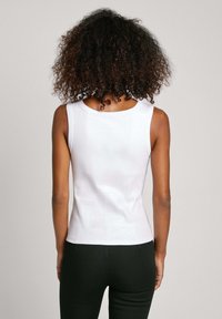 Canottiera bianca a coste con scollo rotondo e design aderente, caratterizzata da una superficie liscia e priva di motivi o accessori visibili.