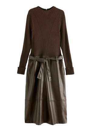Haut marron à manches longues en maille côtelée, associé à une jupe en similicuir marron foncé avec une ceinture nouée à la taille.