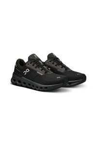 Scarpe sportive nere con tomaia in rete, dotate di un logo grigio a contrasto, suola imbottita e fori di ventilazione visibili per il flusso d'aria e il supporto.