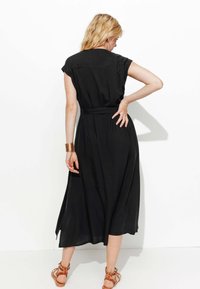 Robe noire, longueur genou avec manches courtes, taille ceinturée et coupe décontractée. Tissu doux et design simple avec un détail de yoke au dos.
