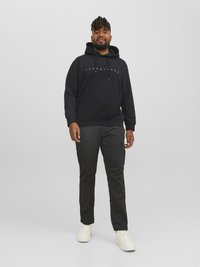 Sort hættetrøje med snørebånd og hvidt logo, parret med mørke cargo-bukser med sidelommer. Modellen har hvide sneakers på.