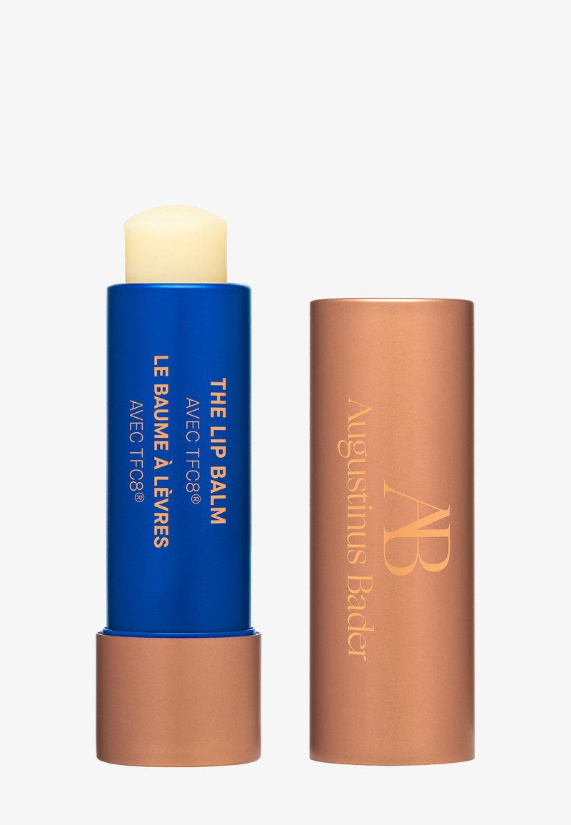 Lippenbalsam-Stift mit blauem Gehäuse und roségoldener Kappe, beschriftet mit „The Lip Balm“ und „Augustinus Bader“ in goldener Schrift.