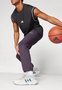 Black sleeveless athletic top with white accents, purple tapered pants, and gray sneakers with blue stripes, holding an orange basketball.