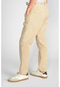 Beige katoenen broek met een ontspannen pasvorm, voorzien van zijzakken en een gestructureerde tailleband, gecombineerd met witte sneakers met een bruine zool.