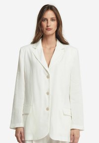 Vit linnes blazer med klassisk slag, tre knappar, två framfickor och avslappnad passform. Strukturerad tyg med en slät yta.