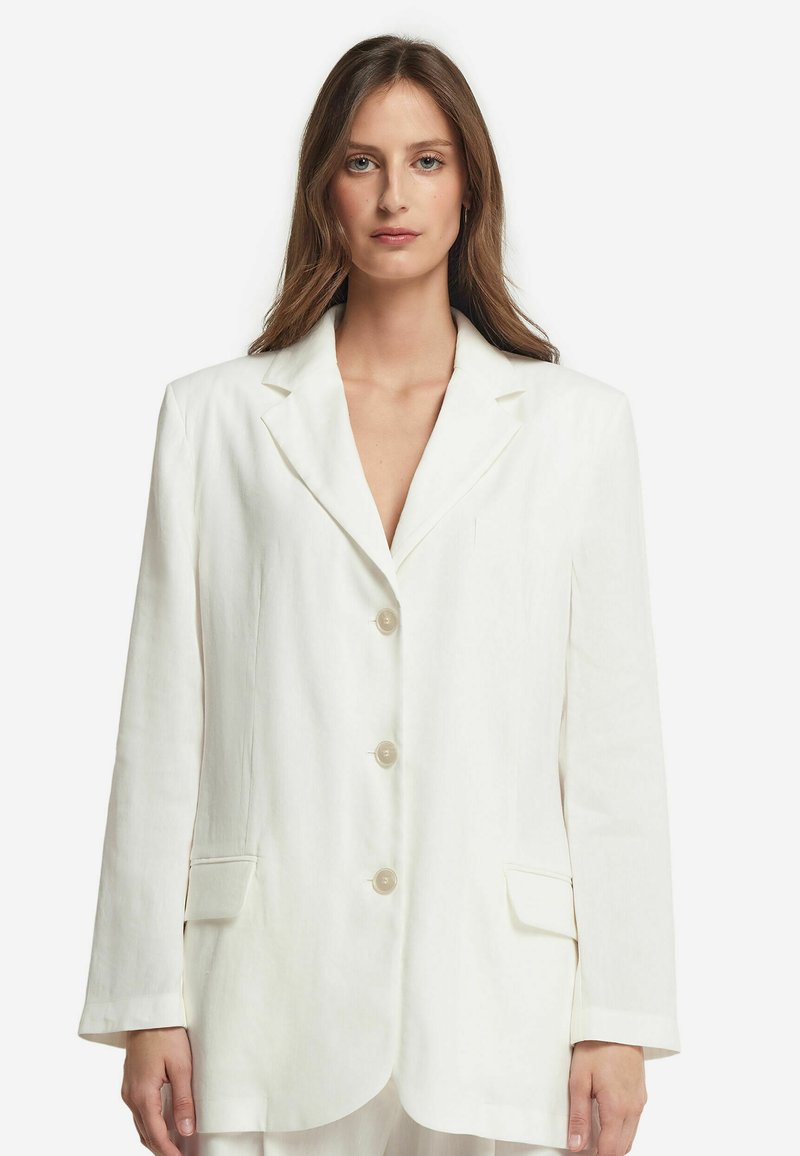 Vit linnes blazer med klassisk slag, tre knappar, två framfickor och avslappnad passform. Strukturerad tyg med en slät yta.