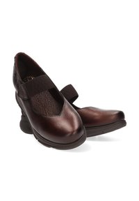 Zapatos Mary Jane de cuero marrón con un acabado texturizado, correa elástica, punta redondeada y un tacón de goma grueso. Diseño estiloso y funcional.