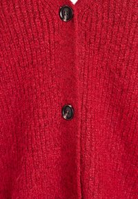 Rdeča pletena kardigan s rebrasto teksturo, v-vratom in dvema črnima gumboma za zapiranje, ki poudarja toplino in udobje.