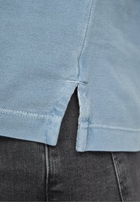 Vaaleansininen puuvillapaita, jossa on teksturoidunnyy finish, kyljissä halkiot helmassa ja suora leikkaus, yhdistettynä tummiin farkkuihin.