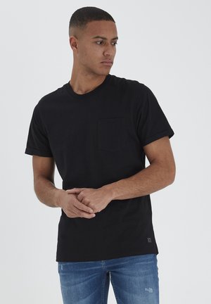 Camiseta de algodón negra con mangas cortas, escote redondo y un bolsillo en el pecho. Presenta un dobladillo en las mangas y un sutil detalle de logo en el dobladillo.