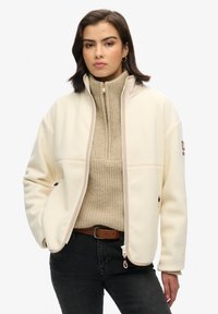 Fleecejack in crèmekleur met een rits aan de voorkant, voorzien van ribben in beige bij de nek en accenten. Inclusief twee zijzakken en een label op de linker mouw.