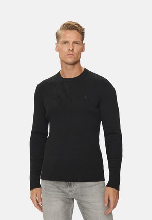 Suéter negro de punto acanalado con cuello redondo y mangas largas. Presenta un sutil detalle del logo en el pecho. Textura suave, diseño ajustado.