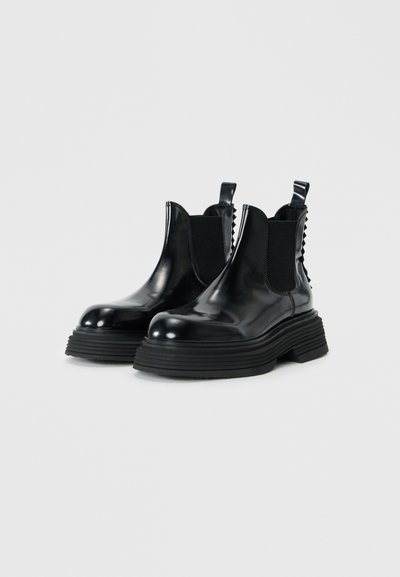 Bottes Chelsea en cuir noir avec des panneaux élastiques sur les côtés, semelles en caoutchouc épaisses et une languette à l'arrière. Fini brillant et accents texturés.
