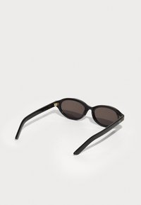 Svarte solbriller med runde linser, mørkebrun tonet glass, og gull hardware-accents på rammen. Glatt plastmateriale med et elegant design.