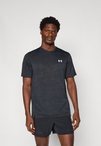 Zwarte sport t-shirt met korte mouwen, textuurstof, subtiel patroon en wit logo op de borst, gecombineerd met zwarte shorts.