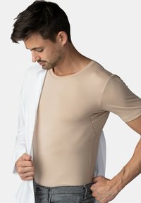 Béžová upnutá košile s krátkým rukávem a kulatým výstřihem, vyrobená z hladkého, elastického materiálu, nošená pod rozepnutou bílou košilí.