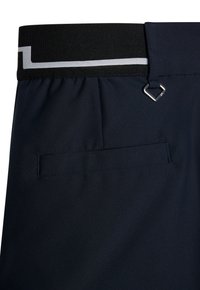 Marina byxor med svart elastiskt midjeband som har en vit rand, bakficka med passpoal och en liten silver D-ring nära bälteslöpet.