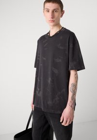 Svart oversized t-skjorte med subtil marmorert tekstur, rund hals og korte ermer. Båret med svarte jeans og en svart veske.