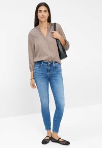 Blouse marron clair à manches longues, coupe ajustée ; jeans skinny bleu moyen ; ballerines noires en toile tissée ; sac à épaule en cuir noir.