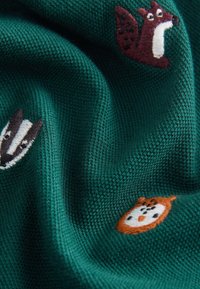 Žalios megztos medžiagos, puoštos siuvinėtomis gyvūnų figūromis: voverę, barsuką ir pelėdą įvairių spalvų. Tekstūra atrodo minkšta ir jauki.