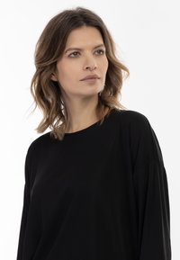 Top nero a maniche lunghe con scollatura rotonda e vestibilità rilassata. Il materiale appare morbido e liscio, cadendo dolcemente sulle spalle.